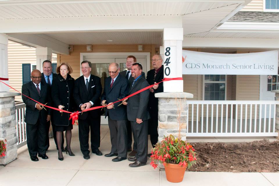 A group of executives cutting the grand opening ribbon outside the new CDS Monarch Senior living home