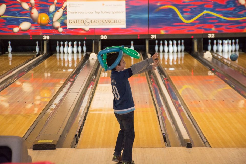 Little boy bowling with balloon animal hat on