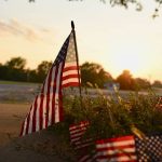 An American flag staked into the grass under the sunset