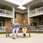 Two women sitting on a bench outside of a senior living home