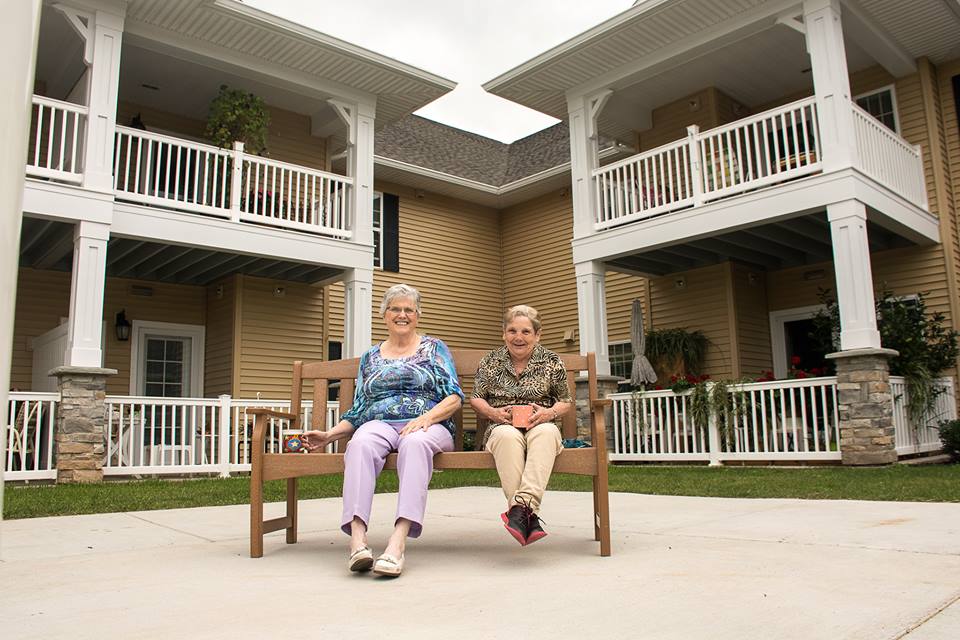 Two women sitting on a bench outside of a senior living home