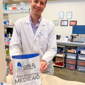 Pharmacist stands behind counter. Sign on counter reads CDS Rx Pharmacy Now Accepting Medicaid.